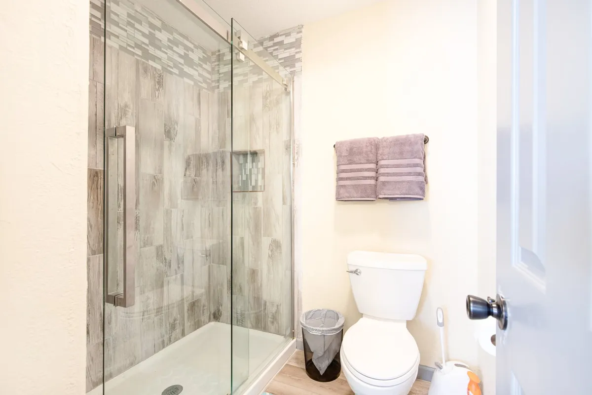 A modern bathroom with a glass shower enclosure, elegant tile work, and fresh towels neatly arranged. The space feels serene and inviting, ready for self-care routines or refreshing showers.
