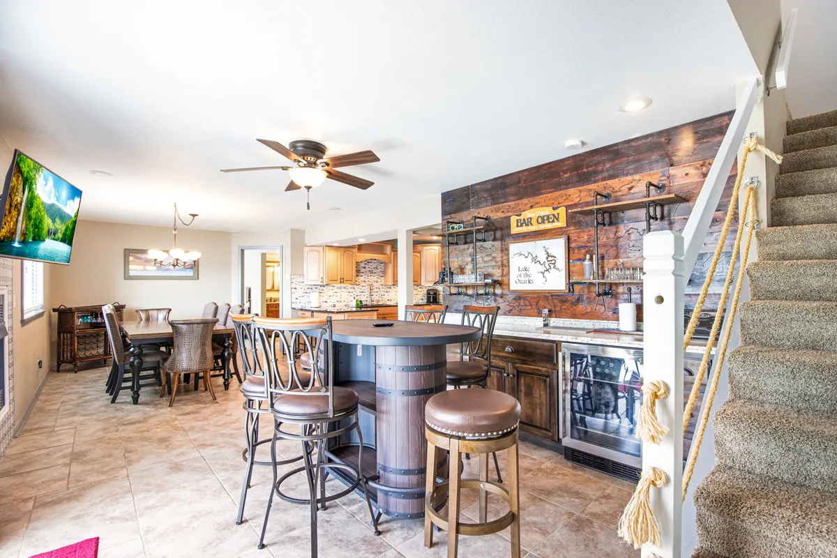 The image features a large, welcoming dining area with a substantial table perfect for group meals, a unique barrel-style counter, and a visible bar. Nautical accents on the staircase further add to the festive, communal vibe, suggesting a space designed for entertaining and sharing meals together.