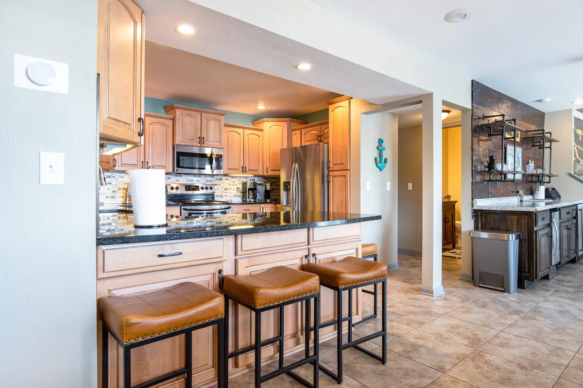 A modern, well-equipped kitchen with a spacious island and bar stools, stainless steel appliances, and stylish backsplash. The kitchen is designed for both cooking and entertaining, inviting guests to gather around while meals are prepared.