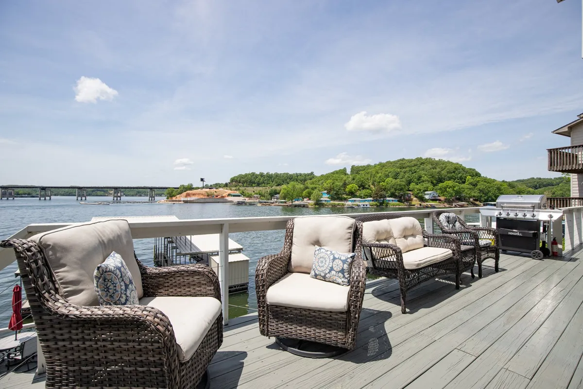 An outdoor patio scene with comfortable wicker chairs facing a grill and a beautiful water view. This setup is tailored for outdoor dining, relaxed conversation, and soaking in the serene lakeside environment—perfect for hosting and entertaining guests outside.
