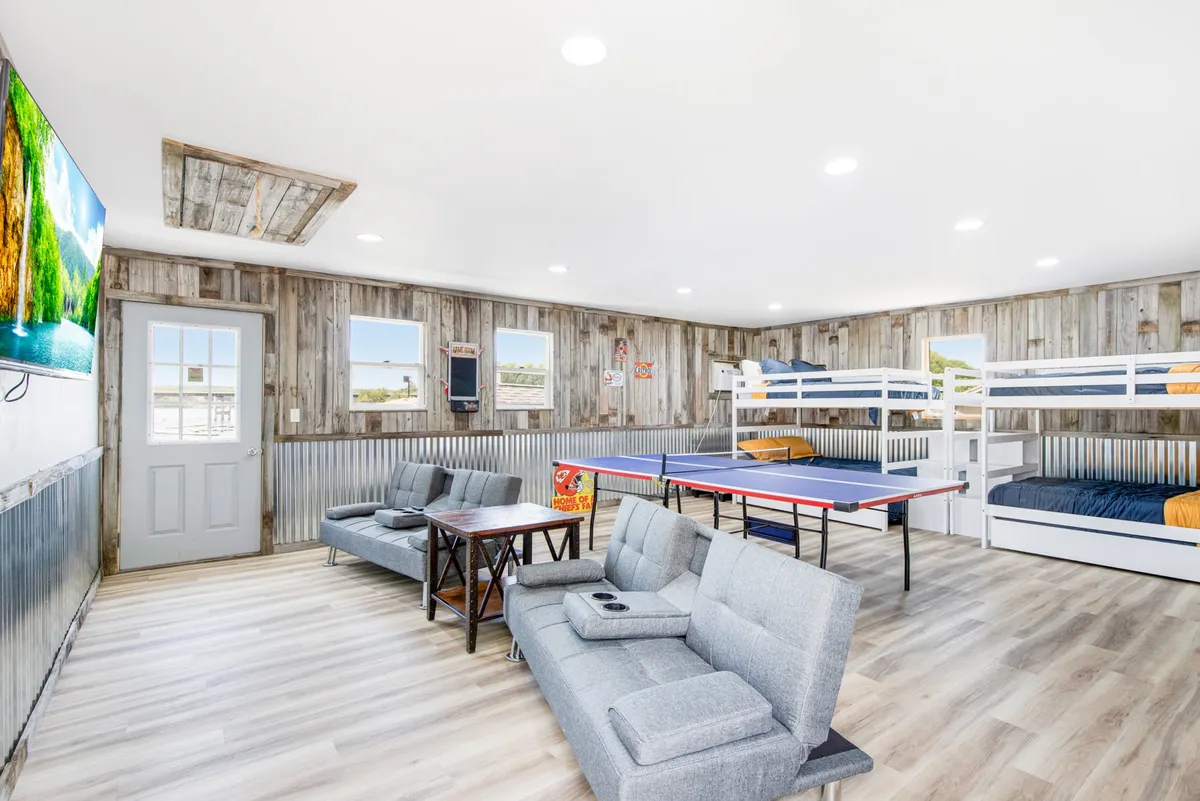 An energetic multi-purpose game and bunk room with bunk beds, comfy sofas, a ping pong table, and a television. The playful layout encourages both relaxation and friendly competition, suitable for all ages.