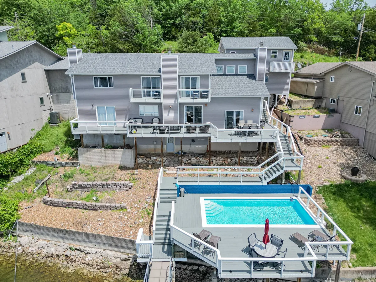 A wide view of the pool and surrounding deck area, framed by lush greenery and balconies. The setup highlights space for swimming, sunbathing, and outdoor gatherings, emphasizing the pool's central role in socializing and summer celebrations.